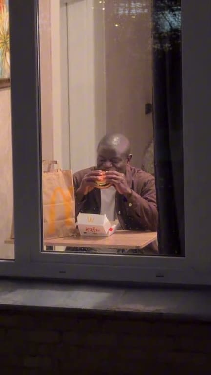 A person takes a late-night burger bite behind an apartment window.